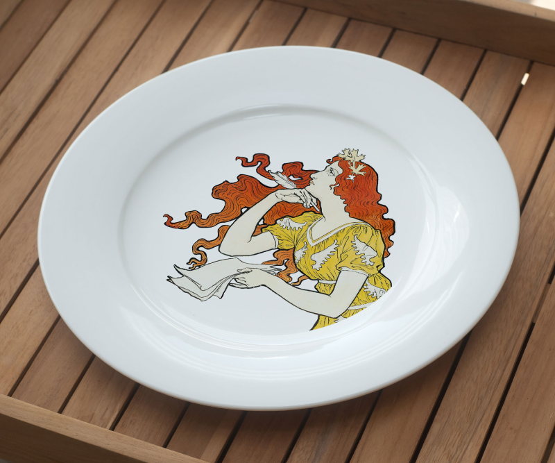 White plate with an Art Nouveau-style illustration of a woman with long red hair wearing a yellow dress