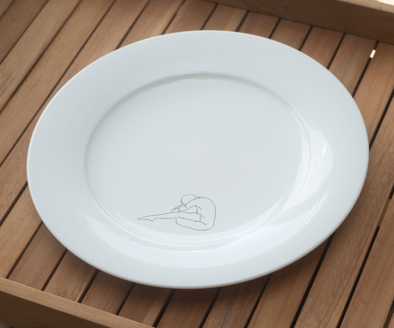 White plate with a minimalist line drawing of a seated nude figure