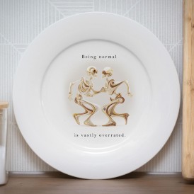 White plate with an illustration of dancing skeletons and the text 'Being normal is really overrated'